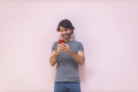 View of a young man with smartphone at daytime on pink wall in the city. High quality photo.