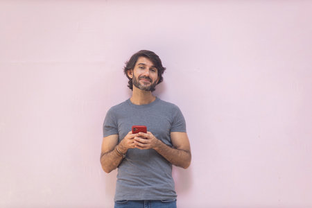 View of a young man with smartphone at daytime on pink wall in the city. High quality photo.