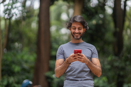View of a young man with smartphone at daytime in a green park in the city. High quality video.の写真素材
