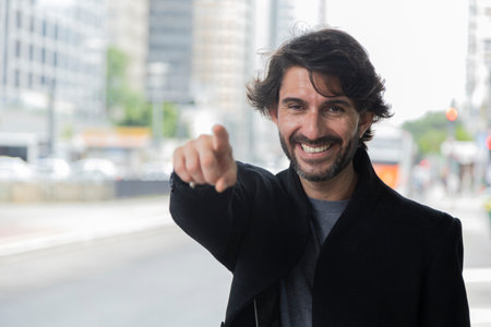 View of a young man pointing and looking at camera at daytime with city landscape in the background. High quality photo.の写真素材
