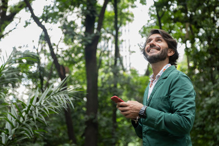 View of a young man with smartphone at daytime in a green park in the city. High quality video.