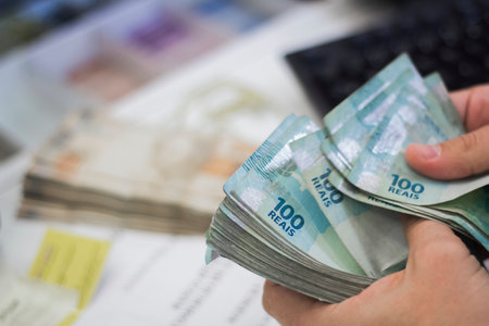 Human hand of businessman working in exchange office / bank. He is counting money and giving cash money to a customer. Brazilian Reais 100 reais bills.の写真素材