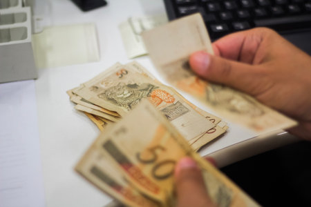 Human hand of businessman working in exchange office / bank. He is counting money and giving cash money to a customer. Brazilian Reais 50 reais bills.の写真素材