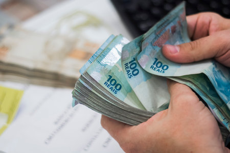 Human hand of businessman working in exchange office / bank. He is counting money and giving cash money to a customer. Brazilian Reais 100 reais bills.の写真素材