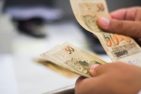 Human hand of businessman working in exchange office/bank. He is counting money and giving cash money to a customer. Brazilian Reais 50 reais bills.の写真素材