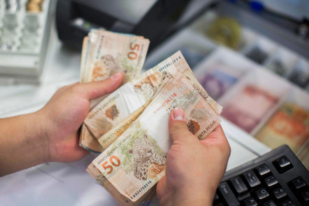 Human hand of businessman working in exchange office / bank. He is counting money and giving cash money to a customer. Brazilian Reais 50 reais bills.の写真素材