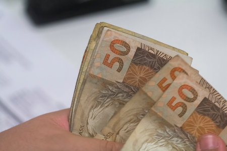 Human hand of businessman working in exchange office / bank. He is counting money and giving cash money to a customer. Brazilian Reais 50 reais bills.の写真素材