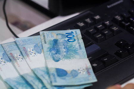 Human hand of businessman working in exchange office / bank. He is counting money and giving cash money to a customer. Brazilian Reais 100 reais bills.の写真素材