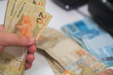 Human hand of businessman working in exchange office/bank. He is counting money and giving cash money to a customer. 20 reais bills.の写真素材