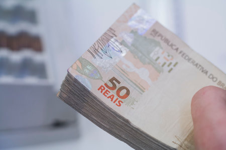 Human hand of businessman working in exchange office / bank. He is counting money and giving cash money to a customer. Brazilian Reais 50 reais bills.の写真素材