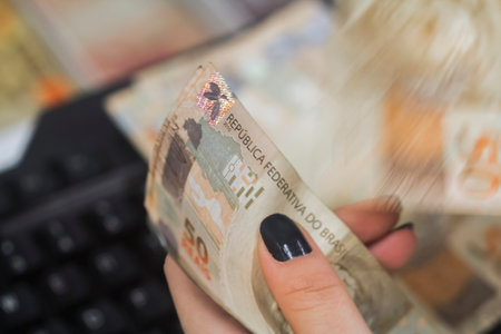 Human hand of businessman working in exchange office / bank. He is counting money and giving cash money to a customer. Brazilian Reais 50 reais bills.の写真素材