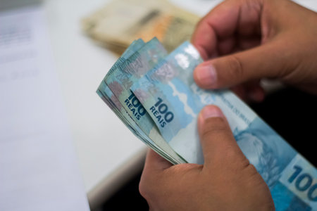 Human hand of businessman working in exchange office/bank. He is counting money and giving cash money to a customer. Brazilian Reais 100 reais bills.の写真素材