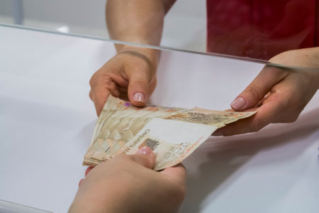 Human hand of businessman working in exchange office/bank. He is counting money and giving cash money to a customer. 50 reais bills.の写真素材