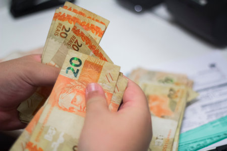 Human hand of businessman working in exchange office/bank. He is counting money and giving cash money to a customer. 20 reais bills.の写真素材