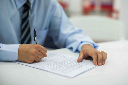 Crop shot of a business person with pen signing document / contract at desk in daylight.