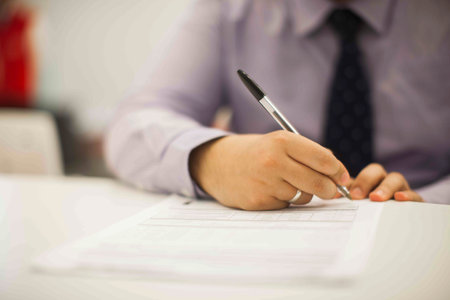 Crop shot of a business person with pen signing document / contract at desk in daylight.の写真素材