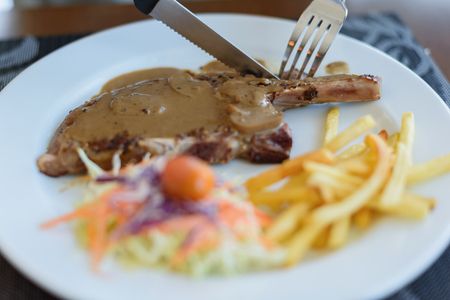 Close-up pork chop steak black pepper with men hand and black pepper sauce in white diskの写真素材