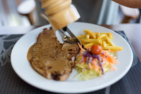 Close-up pork chop steak black pepper with men hand and black pepper sauce in white diskの写真素材
