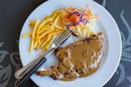 Pork chop steak with black pepper sauce, vegetables and french friesの写真素材