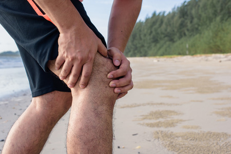 Man running on the beach with knee pain.の写真素材