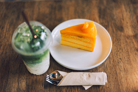 Orange cake, iced matcha green tea latte with milk and spoon on wooden table.の写真素材