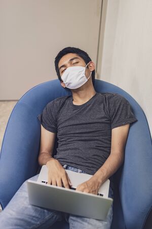 Covid-19, Man wearing face mask sleeping on sofa with laptop computer, Wearing a face mask to protect against coronavirus, business report. Work from home.の写真素材