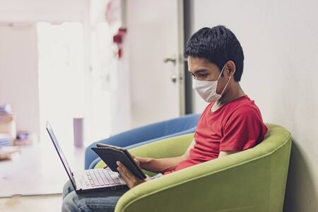 Asian man is working from home during Coronavirus or Covid-19. Wearing a face mask to protect...