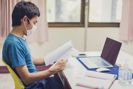 Asian man is working from home during Coronavirus or Covid-19. Wearing a face mask to protect...