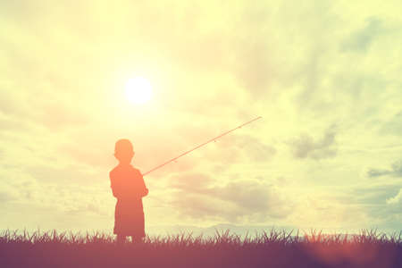 Silhouette grass and little boy fishing with sky and clouds during sunset, Concept of light and shadowの写真素材