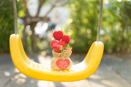 Heart-shaped gifts in a sack on a swing set in sunshine.の写真素材