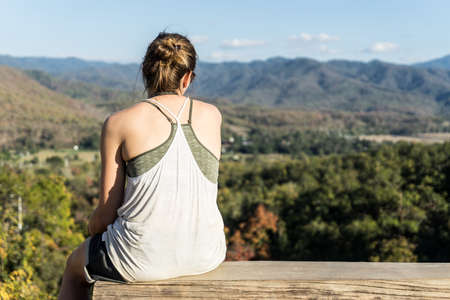 The girl seats on the timber on the mountain alone in sunshine.の写真素材