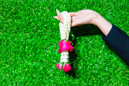 Young girl holding a garland of flowers on a green grass in bright light.の写真素材