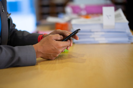 Hands of a man in a gray suit talking on a mobile phone at a desk.