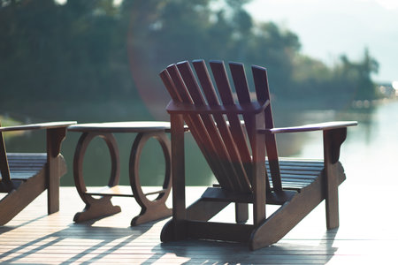 Classic wooden tables and chairs for relaxing by the resort's waterfront in the morning sunlight.の写真素材