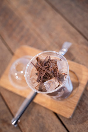 Iced chocolate with chocolate chunks on ice in a glass on a wooden coaster.の写真素材