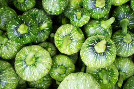 Small green pumpkins are stacked together in large numbers.