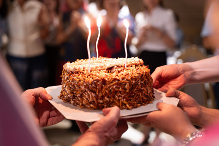 Hands of young people holding a happy birthday cake with their friends Candle flame lights on birthday cake during celebration.の写真素材