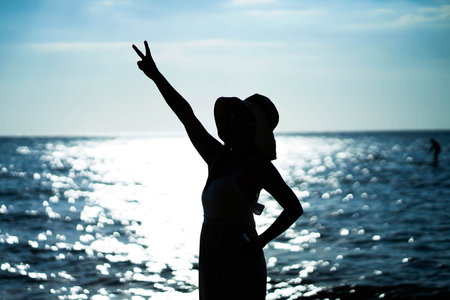 Young woman standing with two fingers up on the beach.の写真素材