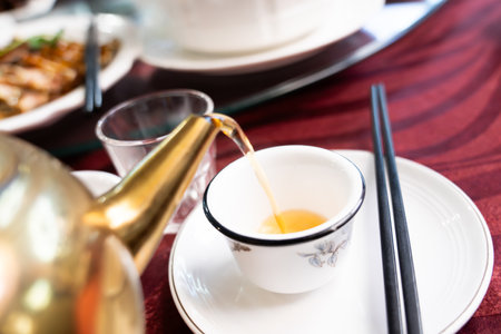 Pour natural chamomile tea from the teapot into the cup on the tableware.の写真素材