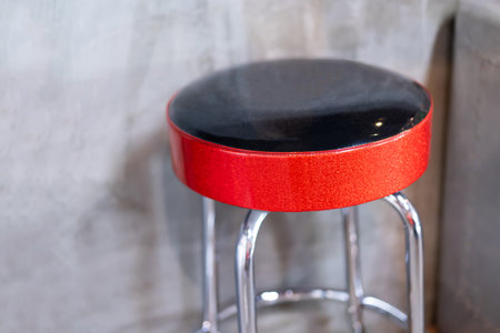 Round high bar stool with red-black leather cushion. In the background was a blurry, empty cement...