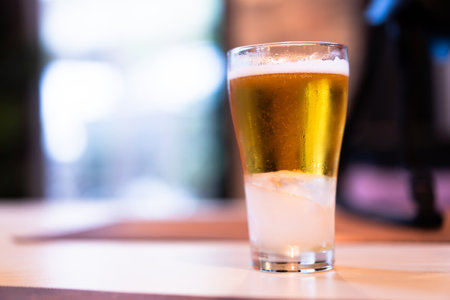 Close-up of cold golden beer in a clear glass on a wooden table, bokeh light background.