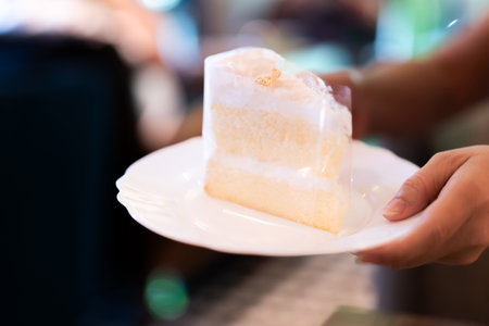 A person serving coconut cake on a white plate in a bakery or coffee shop.