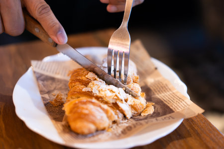 Man eating croissants at wooden table in restaurant. Close-up of cut croissants on plate.の写真素材