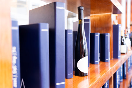 A bottle of wine sits on a shelf next to a row of blue books.の写真素材