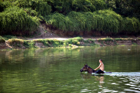 Bucharest, Romania - July 6, 2009: Man and a horse cool down swimming in water.のeditorial素材