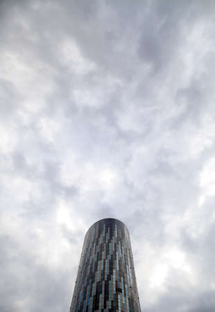 A tall round office building against a cloudy sky