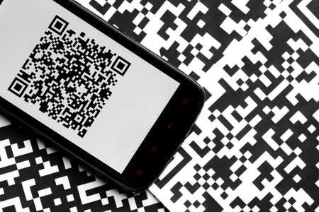 A mobile phone next to some QR codes printed on paperの写真素材
