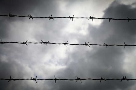 Three lines of barbed wire against a cloudy skyの写真素材