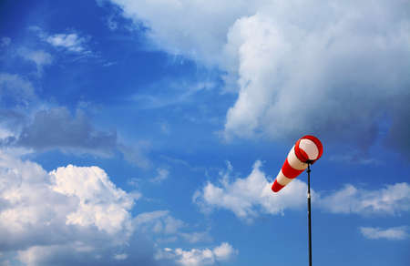 A red wind vane against a blue cloudy sky
