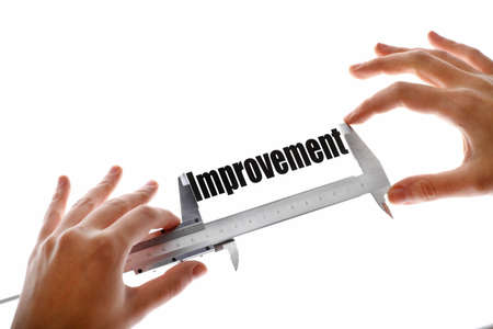 Two hands holding a caliper, measuring the word "Improvement".の写真素材